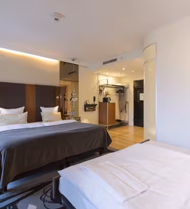 Moderne hotelværelse med to senge, med træaccenter og et stilfuldt tæppe. Værelset har et vægmonteret tv, et skrivebord med en stol og store spejle. Blød belysning og kunstnerisk vægindretning skaber en indbydende stemning.